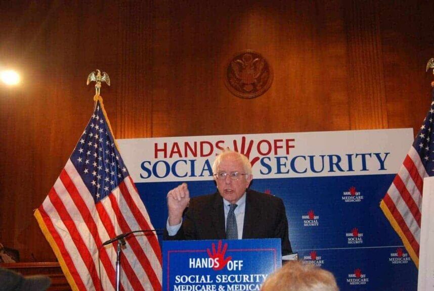 Progressive senator bernie sanders in front of a hands off social security banners
