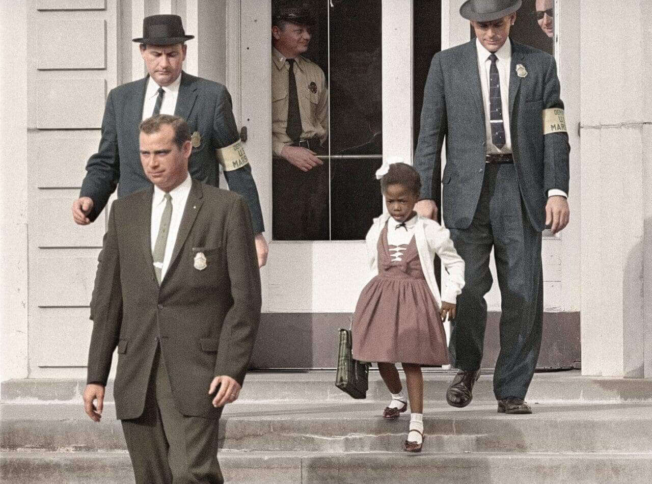 Ruby bridges as a child walking down the steps of a school with three white men around her.