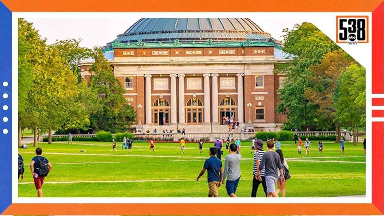 Photo of a college campus with students walking by the building.