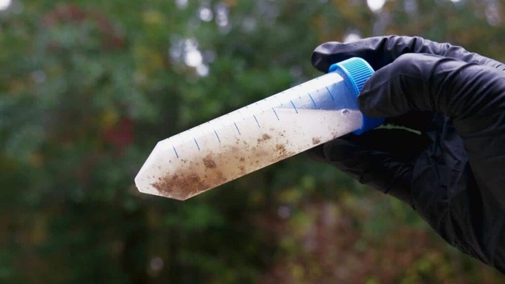 Extremophiles hand wearing black latex gloves holding a vial of a sandy substance