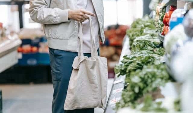 Grocery-shopping Mass deportation man holding a reusable shopping tote looking at green vegetables in a grocery store.