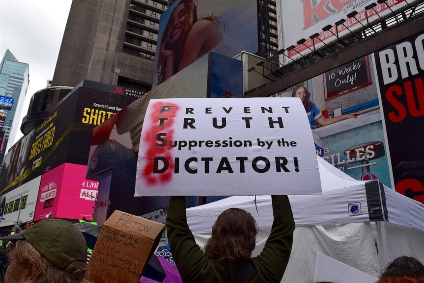 People protested him because donald trump is a fascist. Protester holding a sign spelling out ptsd with d standing for dictator.
