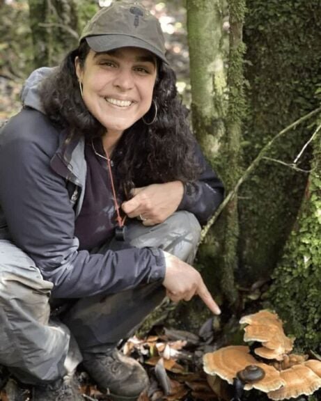Woman in nature pointing to mushrooms.