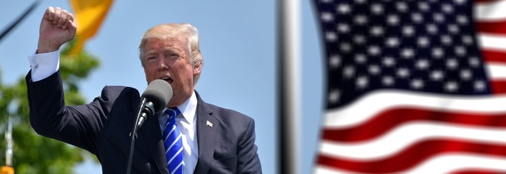 Life In Trump’s America: The Story Of A Once Free Country Authoritarian donald trump raising a fist while shouting into a microphone. The american flag flies beside him.