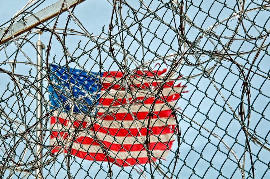 Teen kidnapped by masked ice agents. Razorwire and fencing in front of a torn american flag